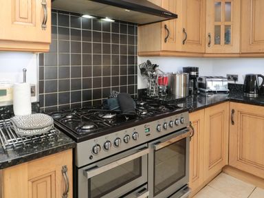 A kitchen with a gas stove and oven black tiled backsplash wooden cabinets and various kitchen appliances at On The Watersedge in Beadnell