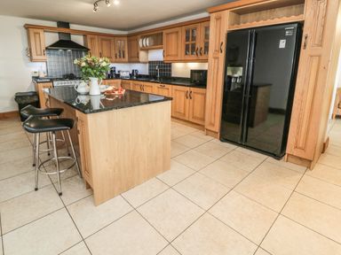 A kitchen with wood cabinets black countertops a black refrigerator and two bar stools at On The Watersedge in Beadnell
