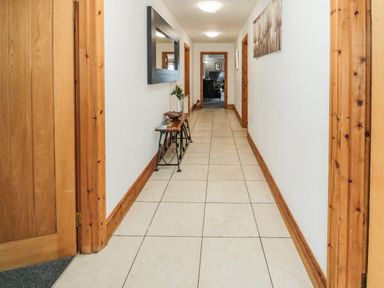 A hallway with tile floor wooden door frames a wall mirror a small table with a plant and magazines and a picture on the wall at On The Watersedge in Beadnell