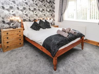 A bedroom with a wooden bed with white bedding and black pillows next to wooden nightstands at On The Watersedge in Beadnell