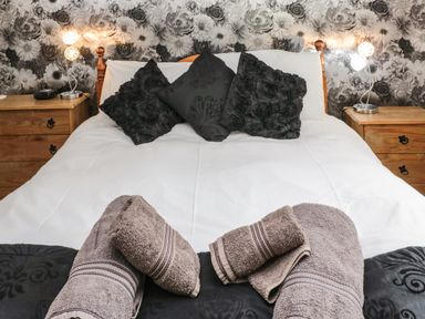 A bedroom with a white bedspread black pillows folded towels on the bed wooden bedside tables with lamps at On The Watersedge in Beadnell