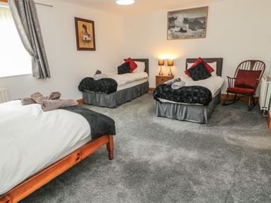 A bedroom with three single beds a wooden chair a nightstand with two lamps and two paintings on the wall at On The Watersedge in Beadnell