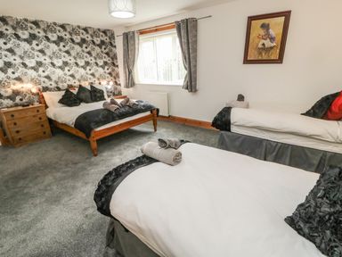 A bedroom with three beds a wooden dresser a window with curtains and floral wallpaper at On The Watersedge in Beadnell