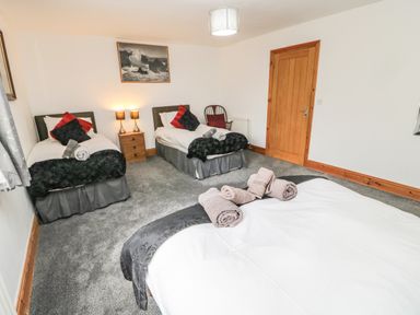 A bedroom with three beds two bedside lamps a wooden door and a carpet at On The Watersedge in Beadnell