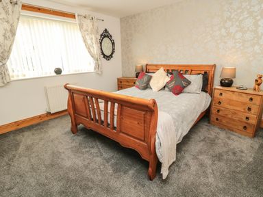 A bedroom with a wooden bed frame gray bedding pillows bedside tables lamps and a window with curtains at On The Watersedge in Beadnell