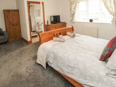 A bedroom with a wooden bed with rolled towels on a bedspread a wooden wardrobe a chest of drawers with a tv and a window with floral curtains at On The Watersedge in Beadnell