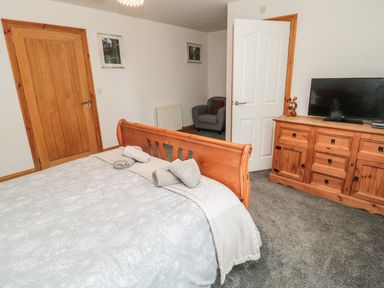 A bedroom with a wooden bed frame a dresser with a TV and a gray armchair at On The Watersedge in Beadnell