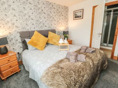 A bedroom with a bed with yellow pillows bedside tables with lamps and an open door leading to a bathroom at On The Watersedge in Beadnell