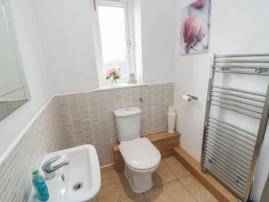 A bathroom with a toilet a sink a window with flowers and a heated towel rail at On The Watersedge in Beadnell