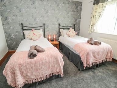 A bedroom with two single beds with pink blankets and floral pillows at On The Watersedge in Beadnell