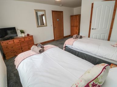 A bedroom with two single beds a wooden dresser with a tv a mirror and a wardrobe at On The Watersedge in Beadnell