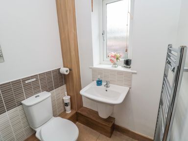 A bathroom with a toilet a sink a window with flowers and a towel radiator at On The Watersedge in Beadnell