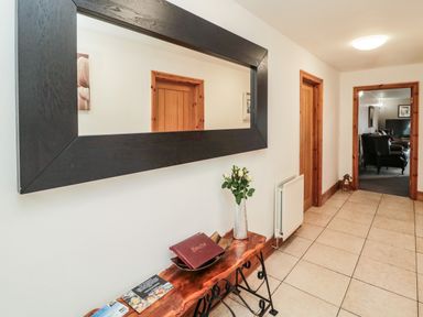 A hallway with wooden doors a large mirror a small wooden table with a vase and book on tiled floor at On The Watersedge in Beadnell