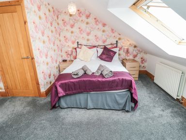 A bedroom with a double bed bedside tables floral wallpaper and a skylight window at On The Watersedge in Beadnell