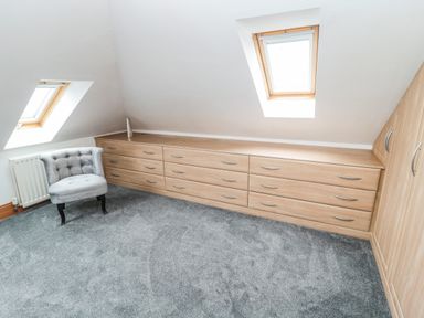 A room with grey carpet a grey upholstered chair wood drawers under two skylight windows at On The Watersedge in Beadnell