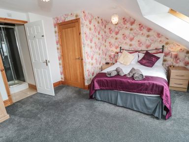A bedroom with a bed with pillows and towels bedside tables and lamps a door leading to a shower at On The Watersedge in Beadnell