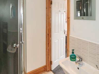 A bathroom with a sink and hand soap next to a shower and an open door at On The Watersedge in Beadnell