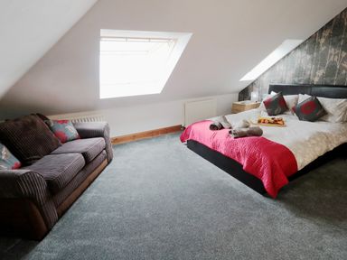 A bedroom with a bed with red and white bedding and a sofa under skylight windows at On The Watersedge in Beadnell