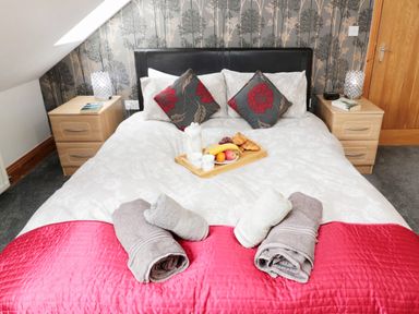 A bedroom with a double bed with pillows and folded towels on a red runner at On The Watersedge in Beadnell
