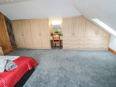 A bedroom with grey carpet wood wardrobe and a chair at On The Watersedge in Beadnell