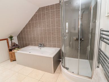 A bathroom with a bathtub shower enclosure and a wooden cabinet at On The Watersedge in Beadnell