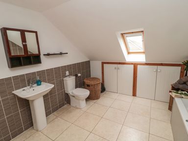 A bathroom with a sink toilet wicker basket skylight and storage cupboards at On The Watersedge in Beadnell