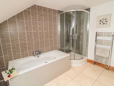 A bathroom with a bathtub a shower with glass doors a wall-mounted towel rack and a framed picture at On The Watersedge in Beadnell