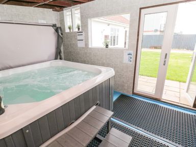 A hot tub inside a tiled room with sliding glass doors opening to a garden at On The Watersedge in Beadnell