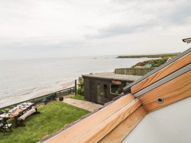 A grassy garden with a picnic table and chairs overlooking the beach and sea at On The Watersedge in Beadnell
