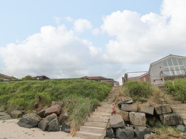 Stone steps leading up from a sandy beach to grassy area with houses and fences at On The Watersedge in Beadnell