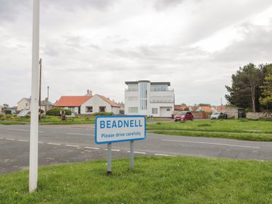 A road sign for Beadnell near houses and parked cars on a cloudy day at On The Watersedge in Beadnell