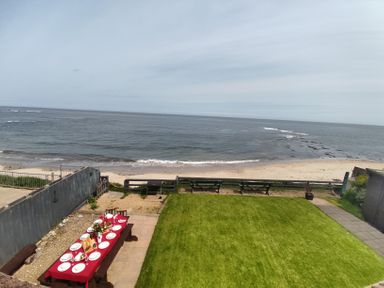 A garden with a table set for a meal on a patio overlooking a beach and ocean at On The Watersedge in Beadnell