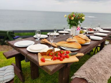 A wooden outdoor dining table with plates glasses bread strawberries and cake by the sea at On The Watersedge in Beadnell