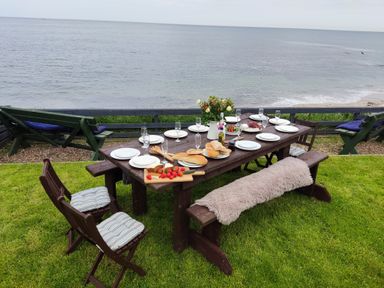 An outdoor dining table set with plates glasses bread and fruit overlooking the sea at On The Watersedge in Beadnell