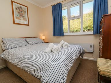A bedroom with a double bed with striped bedding and rolled towels on top at The Shack in Mawgan Porth near Newquay