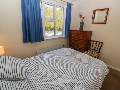 A bedroom with a striped bedspread a wooden chest of drawers a chair and blue curtains at The Shack in Mawgan Porth near Newquay
