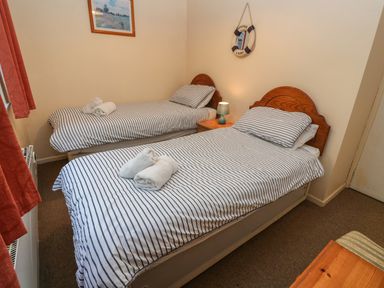A bedroom with two single beds with striped bedding and rolled towels at The Shack Mawgan Porth near Newquay