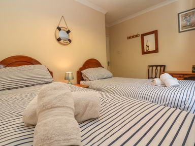 A bedroom with two single beds with striped bedding and rolled towels a lamp a mirror and a desk at The Shack in Mawgan Porth near Newquay