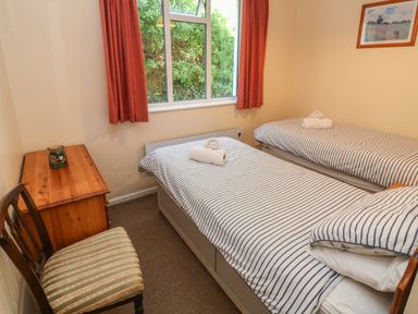 A bedroom with two single beds a wooden chest of drawers and a chair at The Shack in Mawgan Porth near Newquay