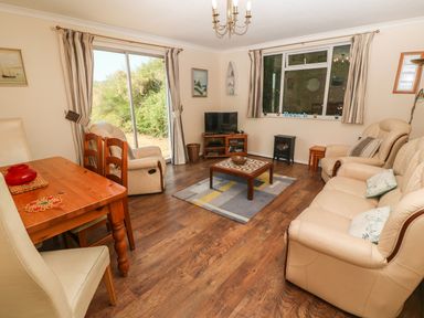 A living room with beige sofas a wooden coffee table a TV on a wooden stand and a dining table at The Shack in Mawgan Porth near Newquay