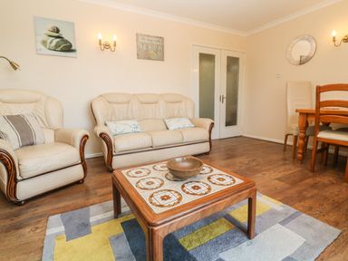 A living room with cream sofas a wooden coffee table and a dining area at The Shack in Mawgan Porth near Newquay