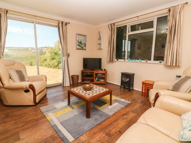 A living room with leather armchairs a wooden coffee table a television and windows with curtains at The Shack in Mawgan Porth near Newquay