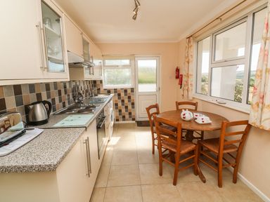 A kitchen with a wooden dining table and chairs next to large windows and cabinets along one wall at The Shack in Mawgan Porth near Newquay