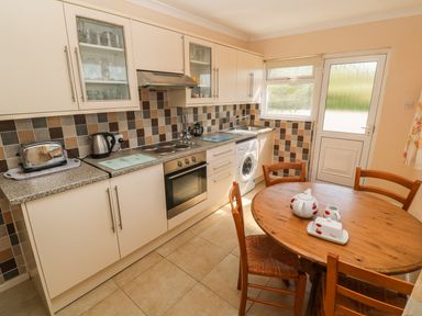 A kitchen with beige cabinets a tiled backsplash a round wooden table with chairs at The Shack in Mawgan Porth near Newquay