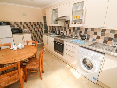 A kitchen with a wooden round table and four chairs a washing machine and oven with cabinets and tiled backsplash at The Shack in Mawgan Porth near Newquay