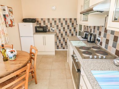 A kitchen with a round wooden table and chairs a refrigerator a microwave an electric stove toaster and kettle at The Shack in Mawgan Porth near Newquay