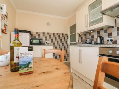 A kitchen with wooden table and chairs a bottle of wine and biscuits on the table a microwave fridge toaster kettle and oven at The Shack in Mawgan Porth near Newquay