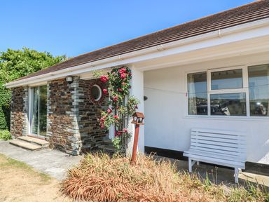 The exterior of a house with a stone and white wall a window a sliding glass door a white bench and a rose bush at The Shack in Mawgan Porth near Newquay