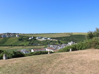 A grassy hill overlooking a village with houses fields and a parking lot at The Shack in Mawgan Porth near Newquay