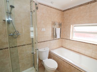 A bathroom with a shower, toilet, bathtub, towel rack, and window at The Shack in Mawgan Porth near Newquay